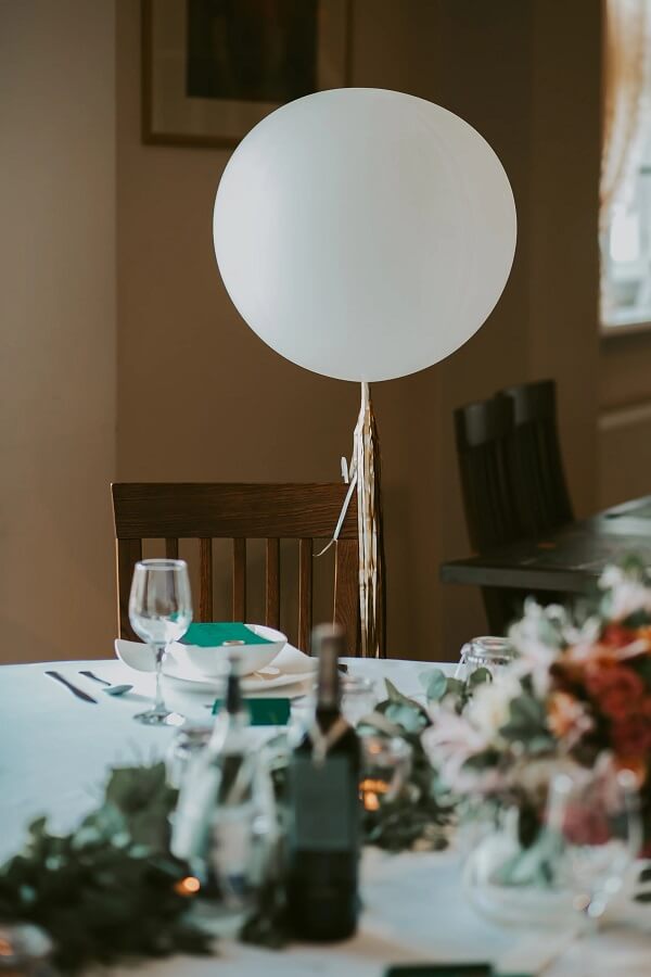 Przystrojony i zastawiony stół przykładowo dla uroczystości weselnej dla gości w sali weselnej z zastawą i białym obrusem. Nad sotłem unosi się biały lampion 